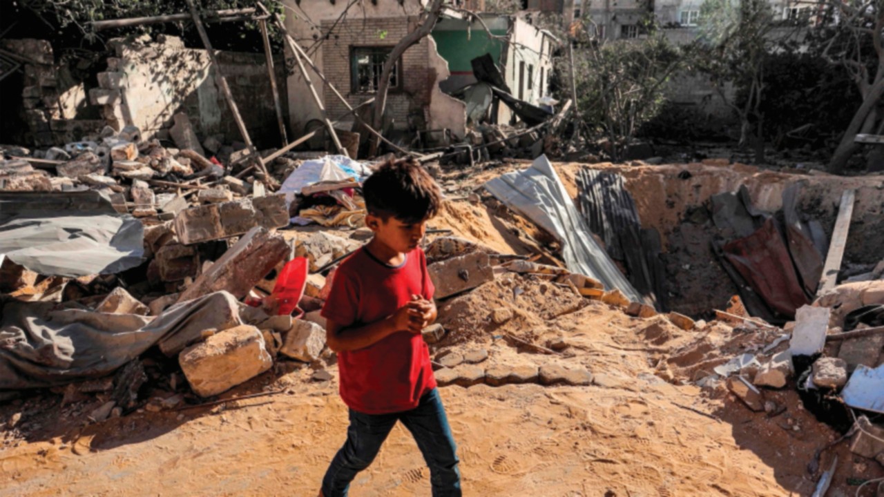 A boy walks past an impact crater at the site of a building that was hit by Israeli bombardment in ...