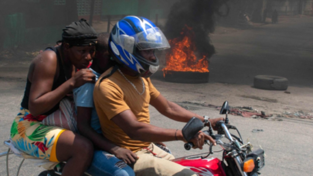 TOPSHOT - A woman with a child lowers her head as they leave the area on a motorcycle after gunshots ...