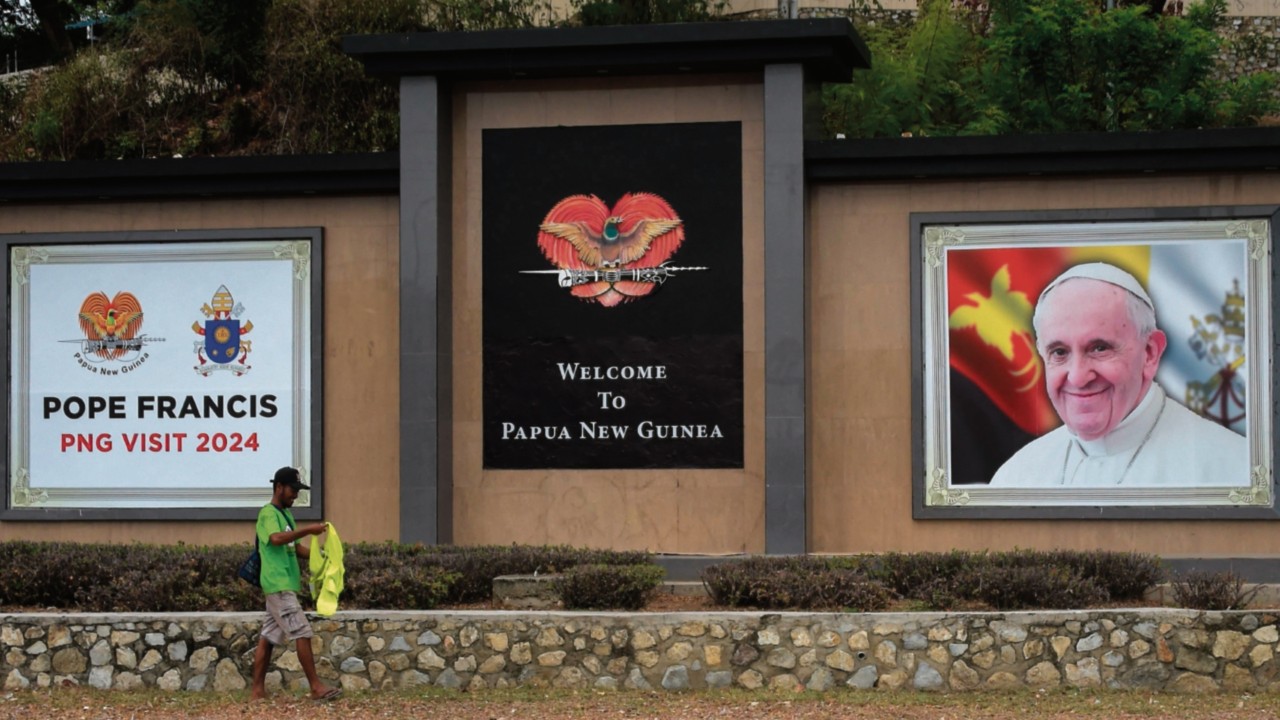 A man walks past a welcome message for Pope Francis displayed on a main road in Port Moresby on ...