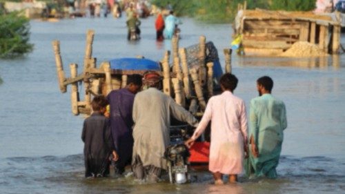 Men walk along a flooded road with their belongings, following rains and floods during the monsoon ...