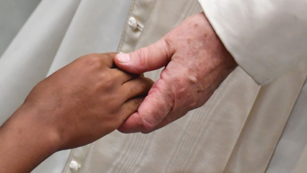 Pope Francis holds a child's hand as he greets sick people during his weekly general audience at ...