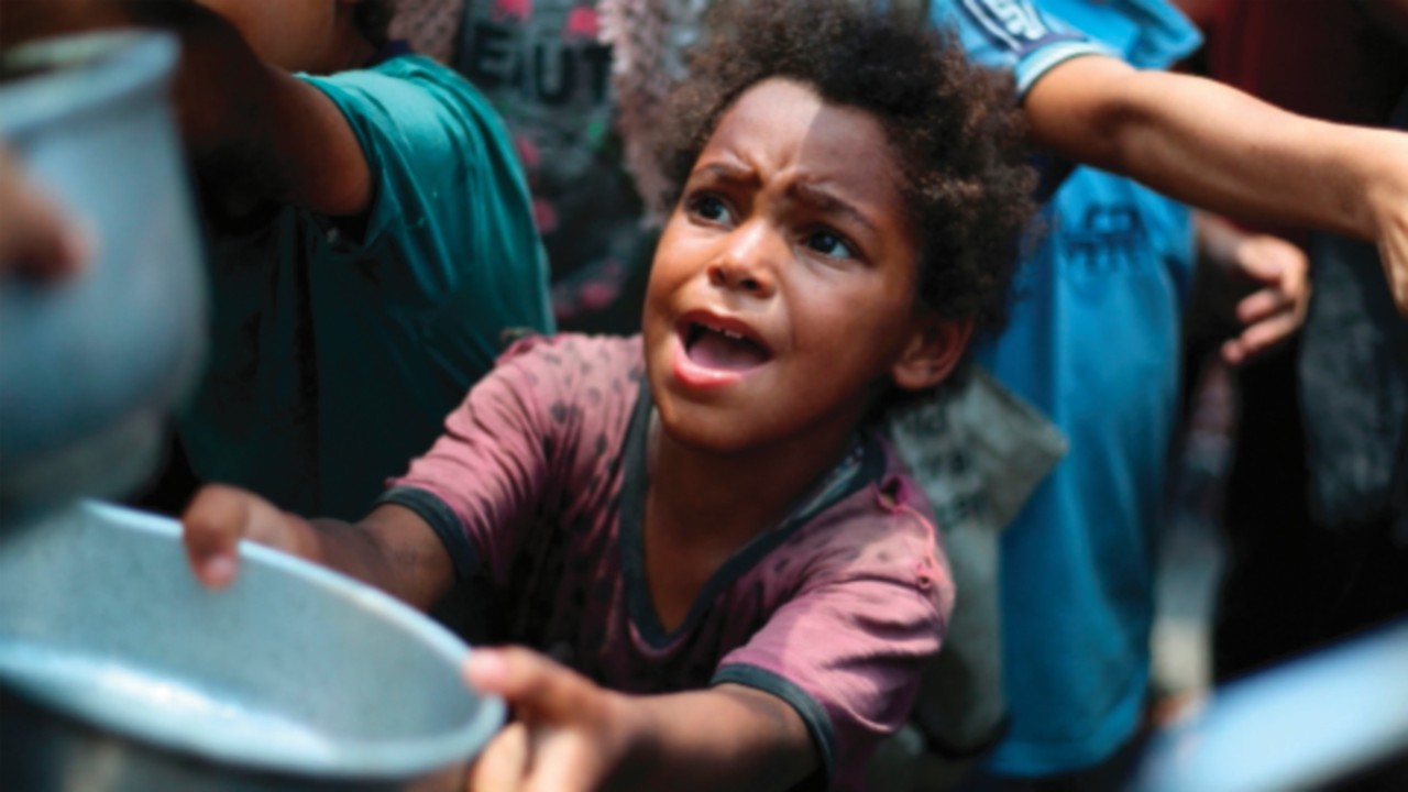 Palestinian children line up to receive a hot meal at a food distribution point in Nuseirat on June ...