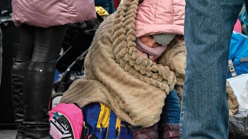 A child wrapped in a blanket sits on luggage while waiting to be relocated from the temporary ...
