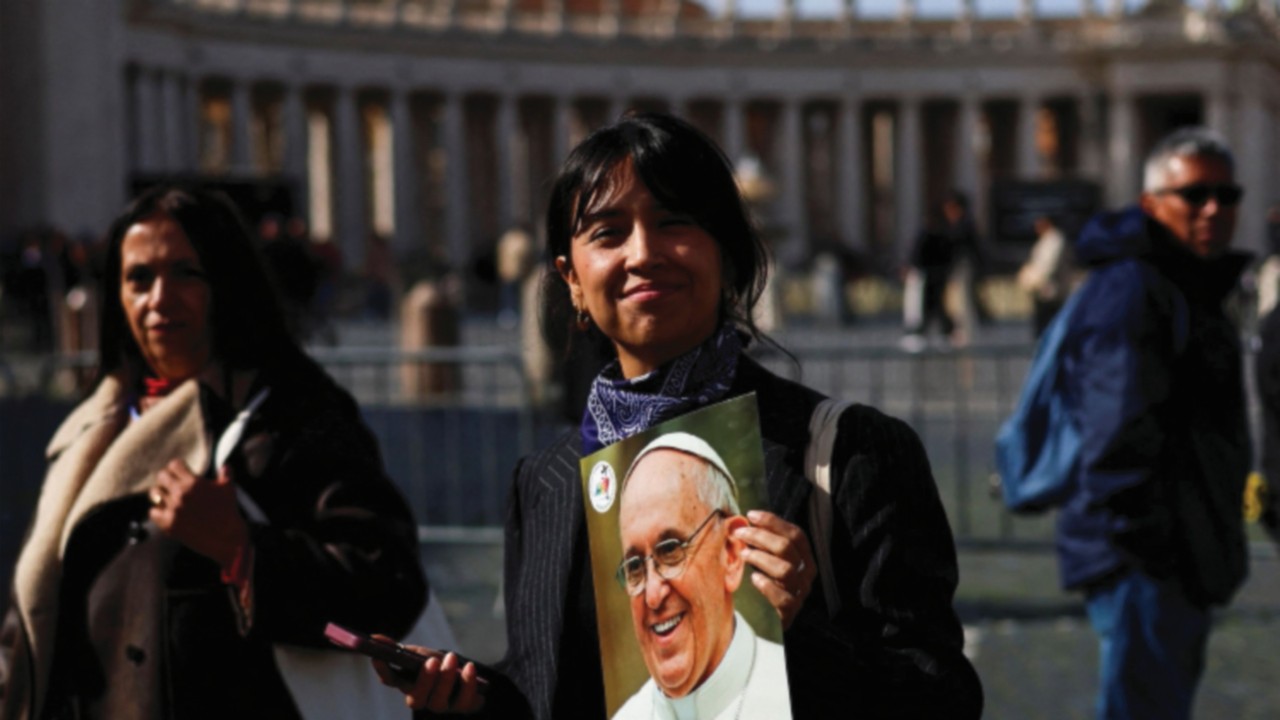 A person holds an image of Pope Francis as he continues his hospitalization, in St. Peter's Square, ...