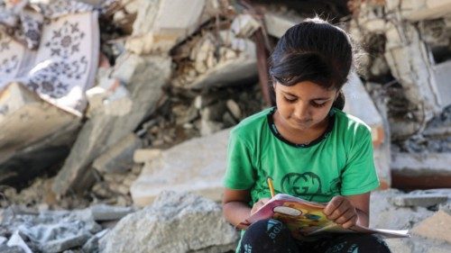 A girl writes in a notebook by the rubble of destroyed buildings near a tent being used as a ...