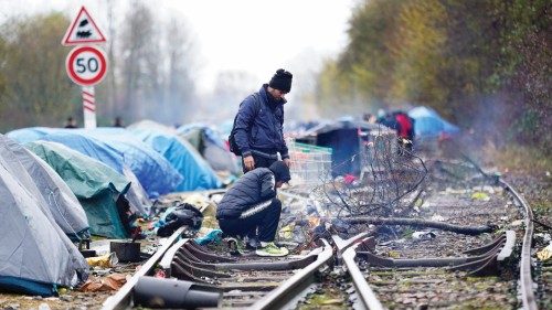Migrants stand near a fire on abandoned train tracks at a makeshift migrant camp at Loon Beach in ...