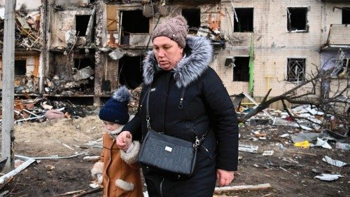 TOPSHOT - A woman with a child walks in front of a damaged residential building at Koshytsa Street, ...