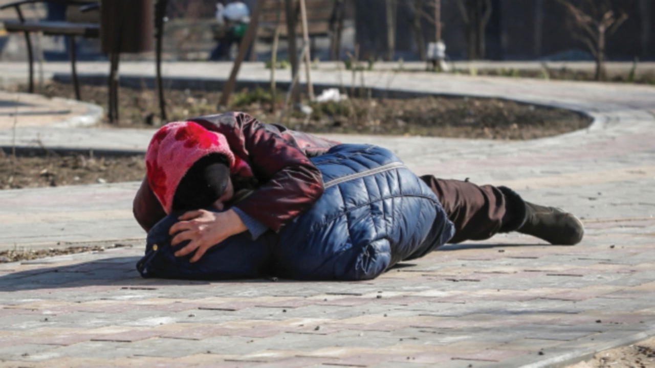 A mother covers her son as they lay on a ground after hearing shelling during Ukraine-Russia ...