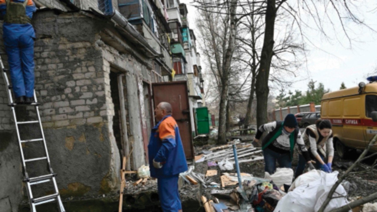 Gas service workers checks a gas pipe as local residents clear debris in a damaged residential ...