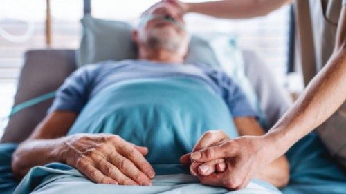 Unrecognizable female doctor examining senior man in bed in hospital, holding hands. Unrecognizable female doctor examining senior man in bed in hospital, holding hands.