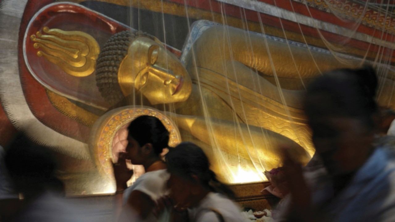 Buddhist devotees worship while walking through the inside of a temple, where Buddha statues have ...