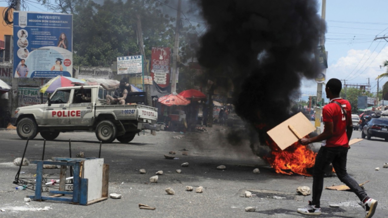 A man holds placards as he yells toward a patrol car near a burning barricade during a protest ...