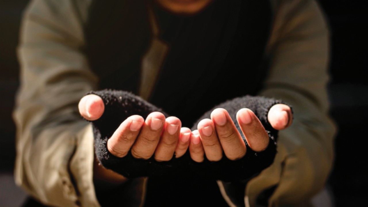 A homeless man begging for help. Ask for a coin of human mercy on a wooden floor in a public ...