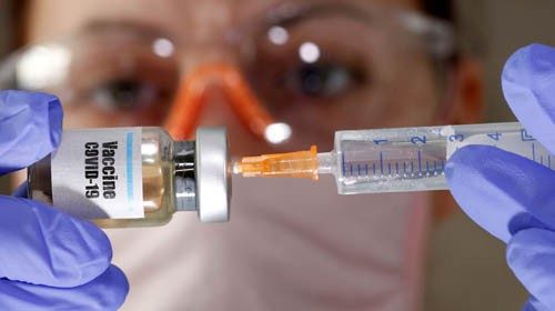 A woman holds a small bottle labeled with a 'Vaccine COVID-19' sticker and a medical syringe in this ...