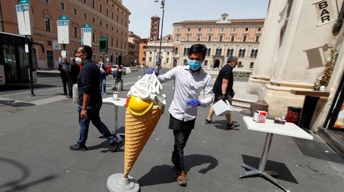 A man wearing a protective mask stands near a figure of an ice cream cone outside a cafe, as Italy ...