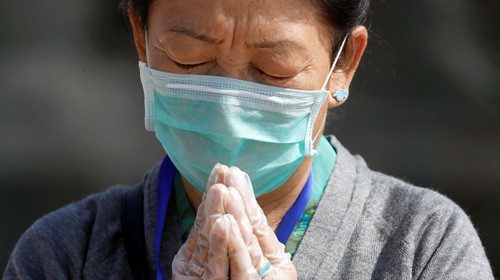 A devotee wearing a protective face mask and gloves offers prayer at Boudhanath Stupa during the ...