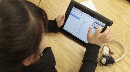 A young girl in a special education classroom reads a worksheet on synonyms uploaded by her teacher ...