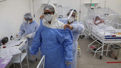 A health worker helps a woman put on protective gear at the Intensive Care Unit for COVID-19 of the ...