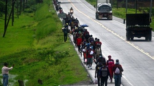 TOPSHOT - A man (L) waves at migrants heading in a caravan to the border with Guatemala along the ...