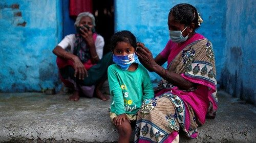 A woman wearing a protective face mask adjusts her daughter's face mask outside their house at a ...