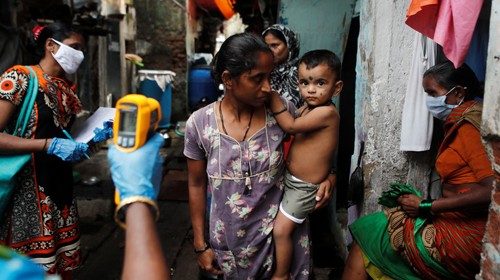 A healthcare worker checks the temperature of residents of a slum area using an electronic ...