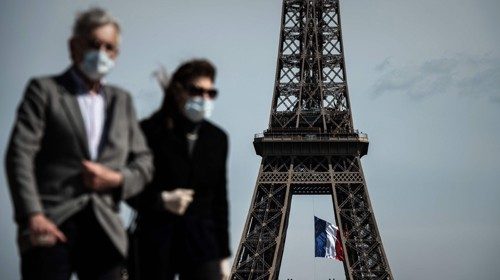 Persone con mascherina passeggiano accanto alla Tour Eiffel (Afp)