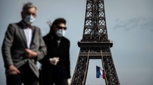 Persone con mascherina passeggiano accanto alla Tour Eiffel (Afp) Persone con mascherina passeggiano accanto alla Tour Eiffel (Afp)
