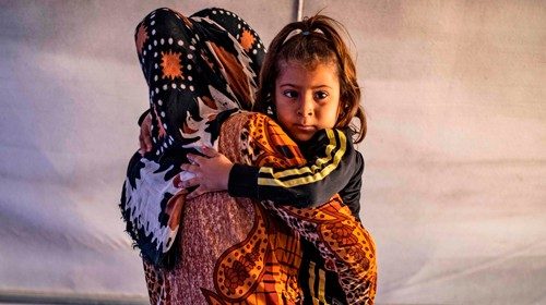 Sfollati siriani. Una donna porta in braccio la figlia di 5 anni paralizzata (Afp)