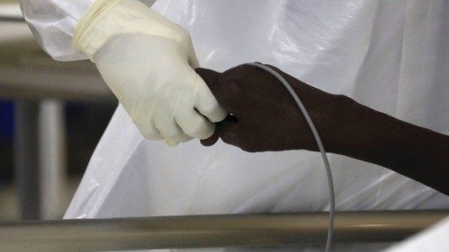 A member of the medical staff dressed in a protective suit holds the hand of a coronavirus disease ...