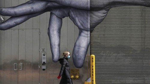 (FILES) In this file photo taken on April 22, 2020 a woman in a mask walks past a mural of a hand on ...