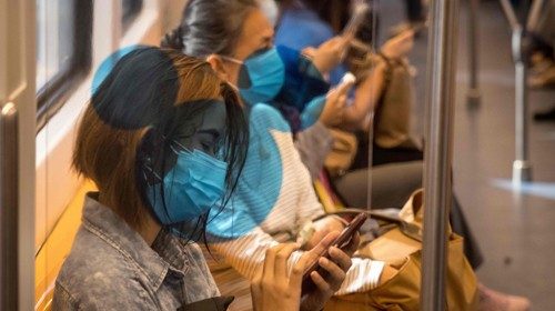 A woman wearing a face mask checks her mobile phone on a BTS commuter train in Bangkok on January 4, ...