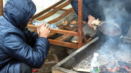 epa08914391 A migrant warms by the fire during a winter day at the Lipa refugee camp outside Bihac, ...