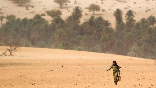 A young girl carries an empty container as she walks across the sands to fill it from a well in ...
