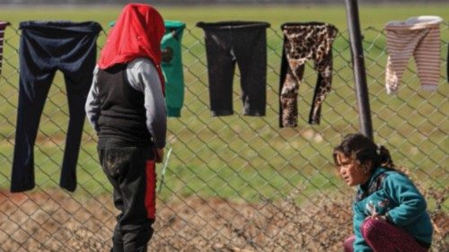 Girls are seen next to laundry hanging to dry on a wire fence at a camp sheltering Syrians displaced ...