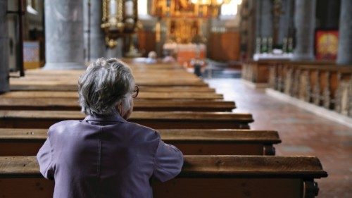 Older woman praying in an almost empty church. Shallow DOF, focus is on the woman