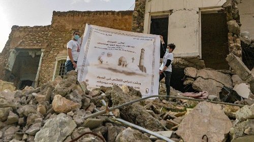 TOPSHOT - Youths unfurl a poster welcoming Pope Francis above the rubble of a destroyed house next ...