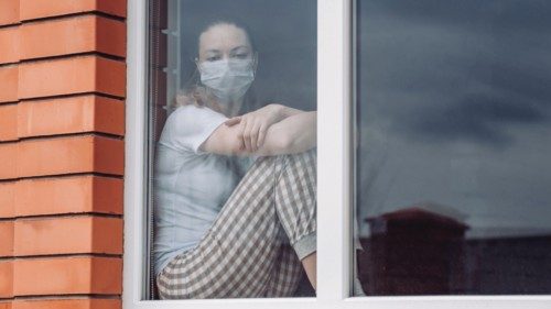 Home quarantine. Caucasian woman sitting at window in a medical mask, looking out, wants to go out. ...