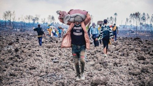 epa09234046 A Congolese porter helps people evacuate across cooled lava from the town of Goma in the ...