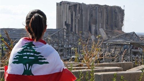 A Lebanese youth wrapped in the national flag looks at the damaged grain silos at Beirut's port, on ...