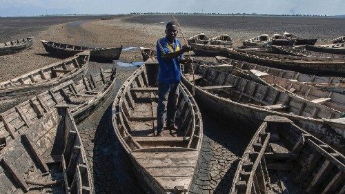 A young man stands among stationary engineless boats which lie idle at the dried inland Lake ...