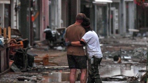 A couple hug as they stand amongst debris left by flood waters in a street in the town of ...