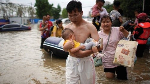 A man holding a baby wades through a flooded road following heavy rainfall in Zhengzhou, Henan ...