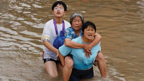 A woman carries an elderly woman as they make their way through floodwaters following heavy rainfall ...