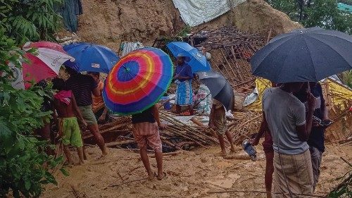 Onlookers stand as Rohingya refugees work amid the debris of houses in Balukhali camp on July 27, ...