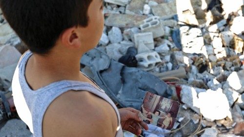 TOPSHOT - A boy holds a personal photo print showing children as he stands by rubble in the ... TOPSHOT - A boy holds a personal photo print showing children as he stands by rubble in the ...
