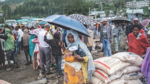 A woman stands with an umbrella next to sacks of rice during a food distribution for internally ...