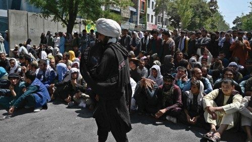 A Taliban fighter walks in front of people sitting along a road outside a bank waiting to withdraw ...