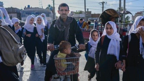 A man along with a child rides a bicycle past school girls walking back to their home in Kabul on ...