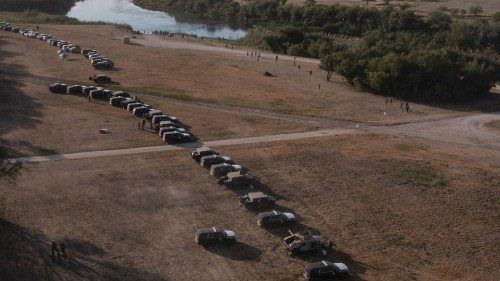 Military and law enforcement vehicles create a cordon around migrants sheltering in a nearby ...