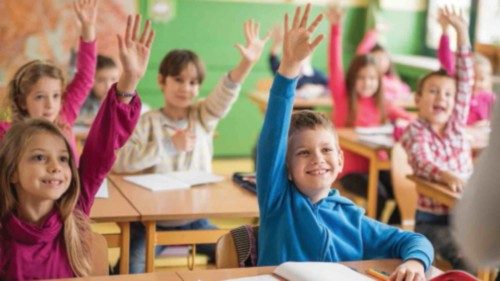 Large group of school children raising their hands ready to answer the question.